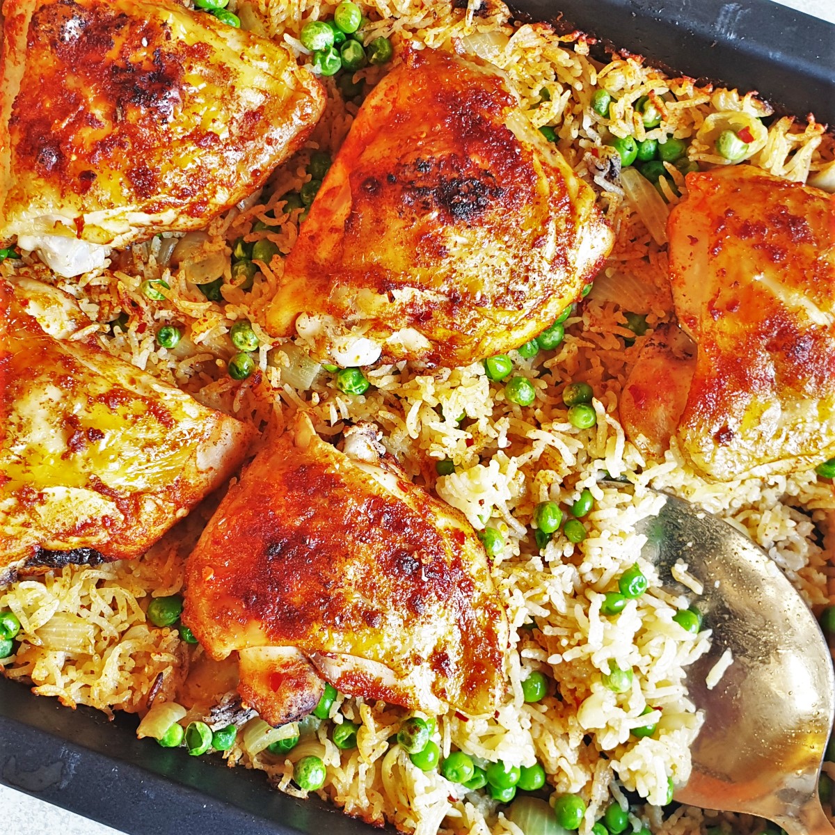 Garlic chicken ovenbake on a bed of peas and rice in a baking dish.