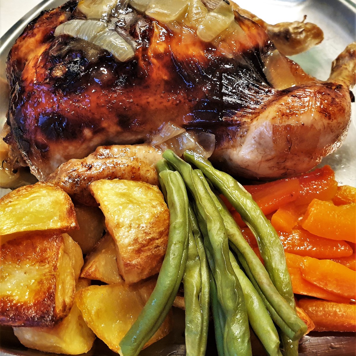 A honey lemon roast chicken on a plate with vegetables.