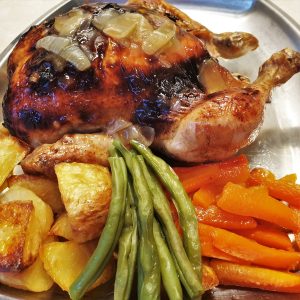 A honey lemon roast chicken on a plate with vegetables.