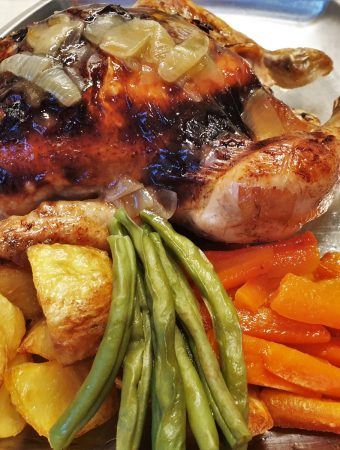 A honey lemon roast chicken on a plate with vegetables.