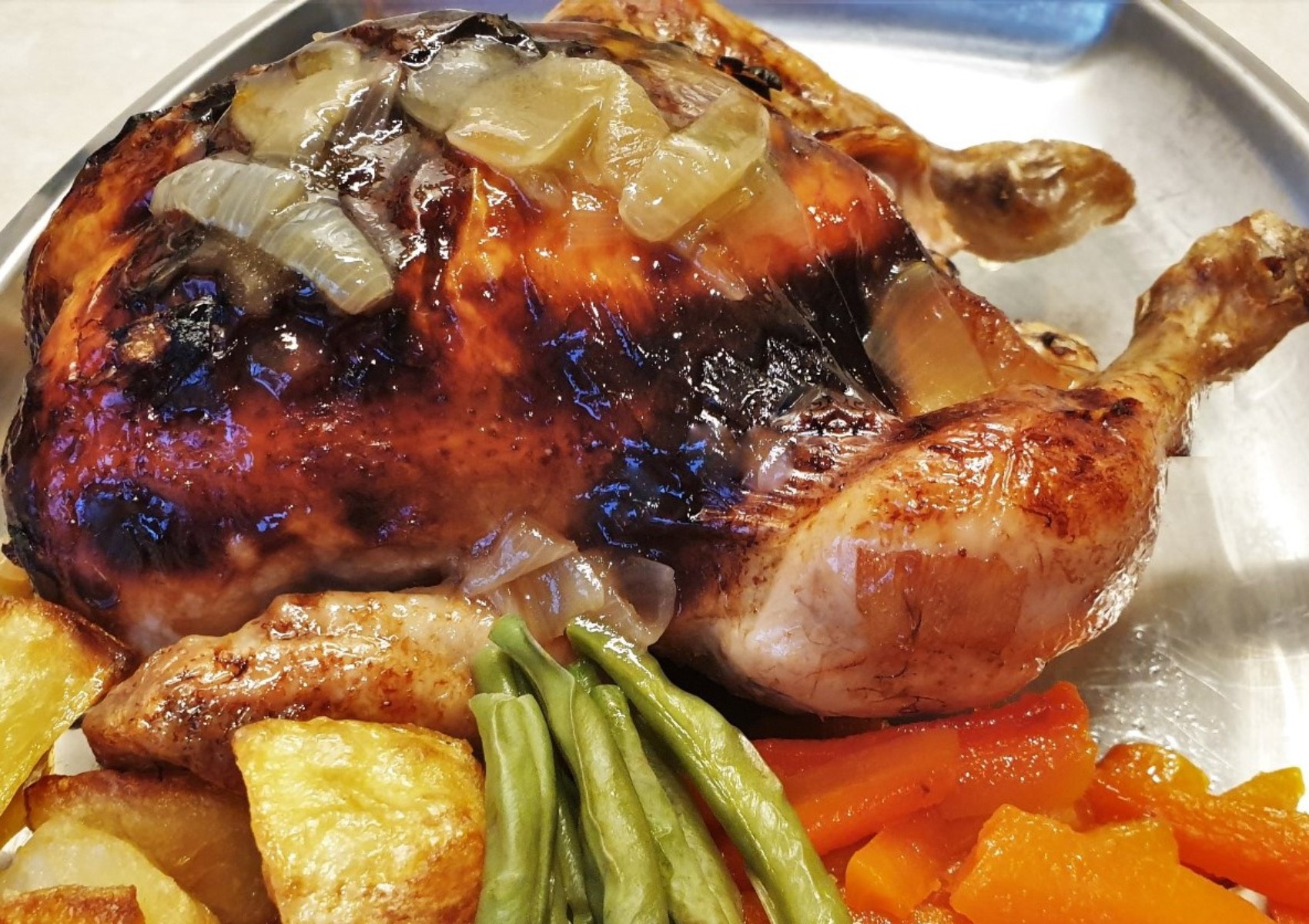A honey lemon roast chicken on a plate with vegetables.