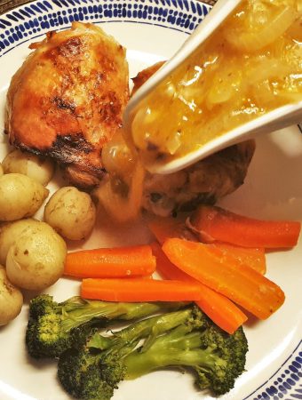 Chicken thighs and vegetables on a plate, with sauce being poured over.