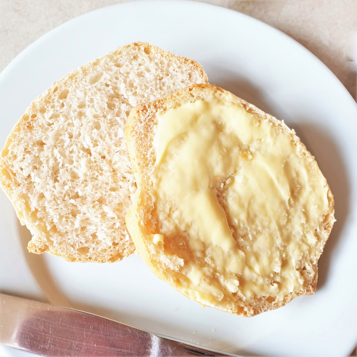 A breadroll split open and spread with butter on a white plate.