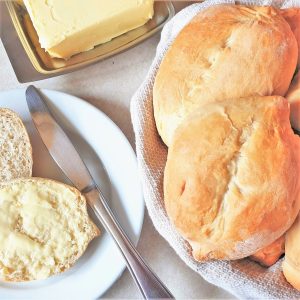 Two Portuguese rolls on a plate next to a roll that has been split open and smeared with butter.