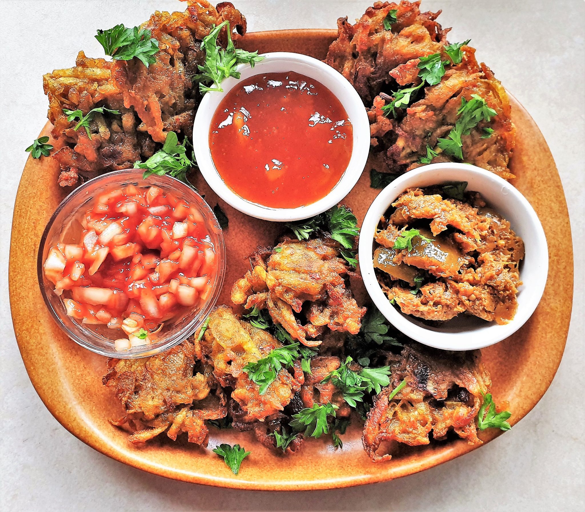 A plate of potato and onion bhajis with dipping sauces.