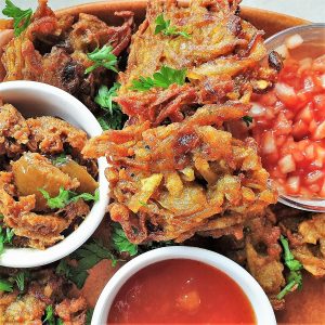 Close up of a potato and onion bhaji with dipping sauces.