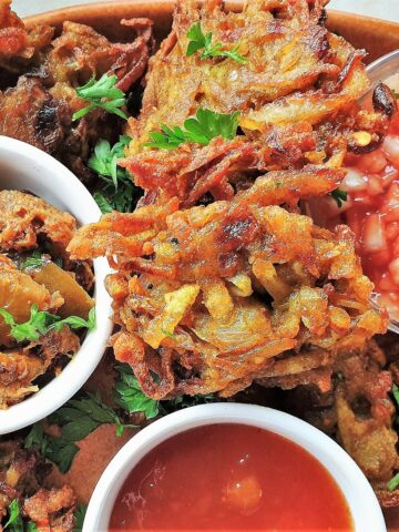 Close up of a potato and onion bhaji with dipping sauces.