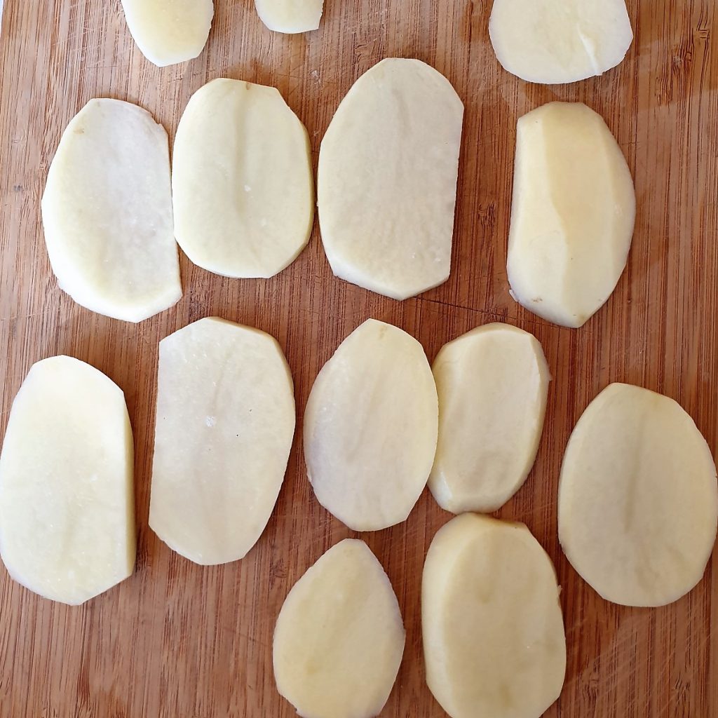 Sliced potatoes on a wooden board.