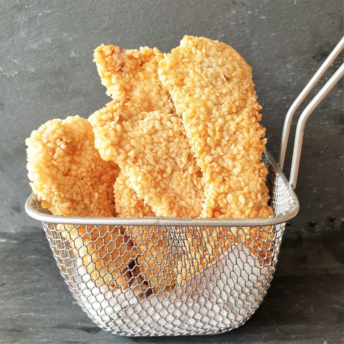 Sesame chicken goujons in a small wire basket.