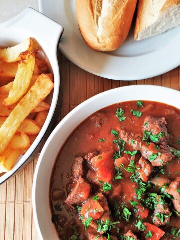 A bowl of beef trinchado next to a bowl of french fries.