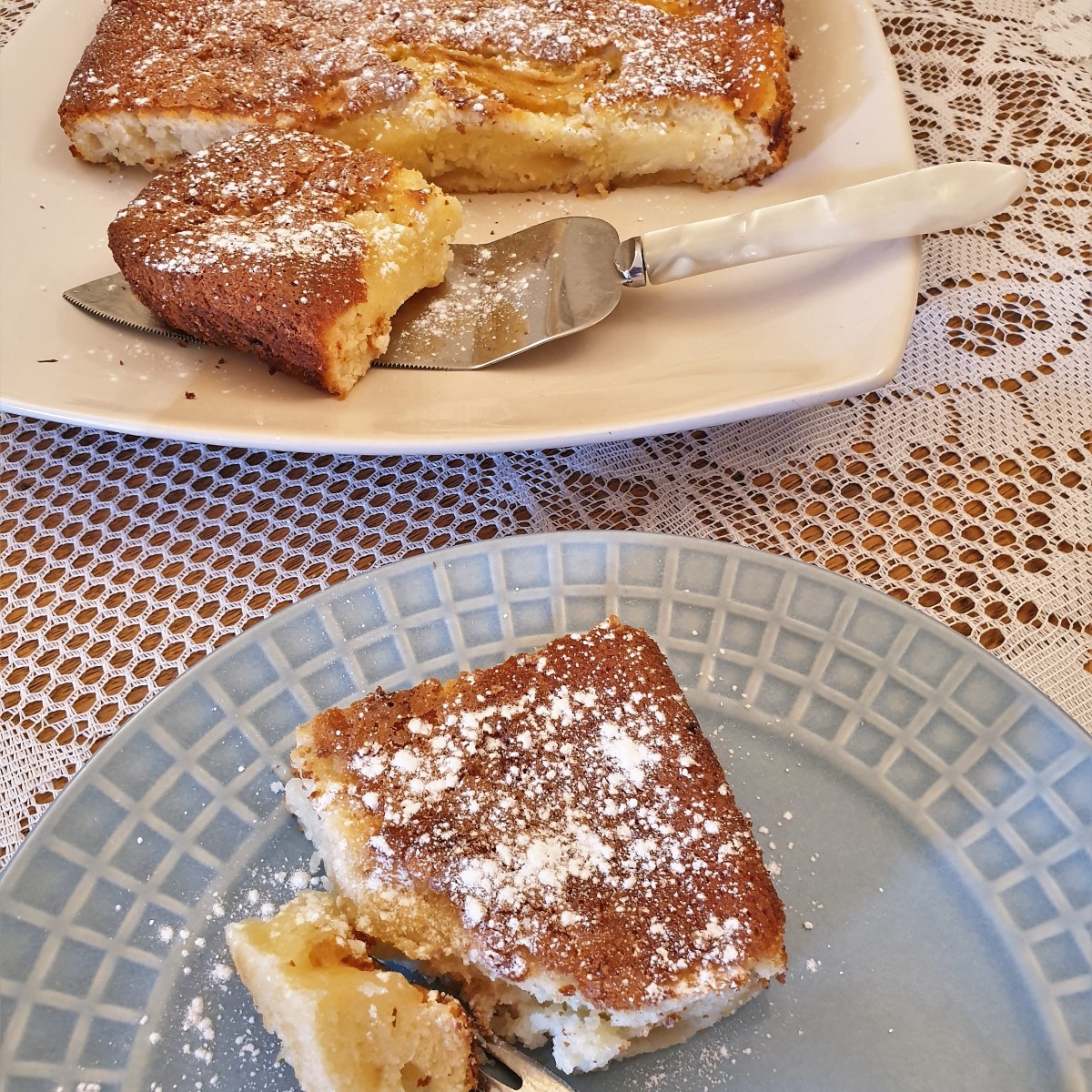 A slice of fresh pear cream slice on a plate with the rest of the cake in the background.