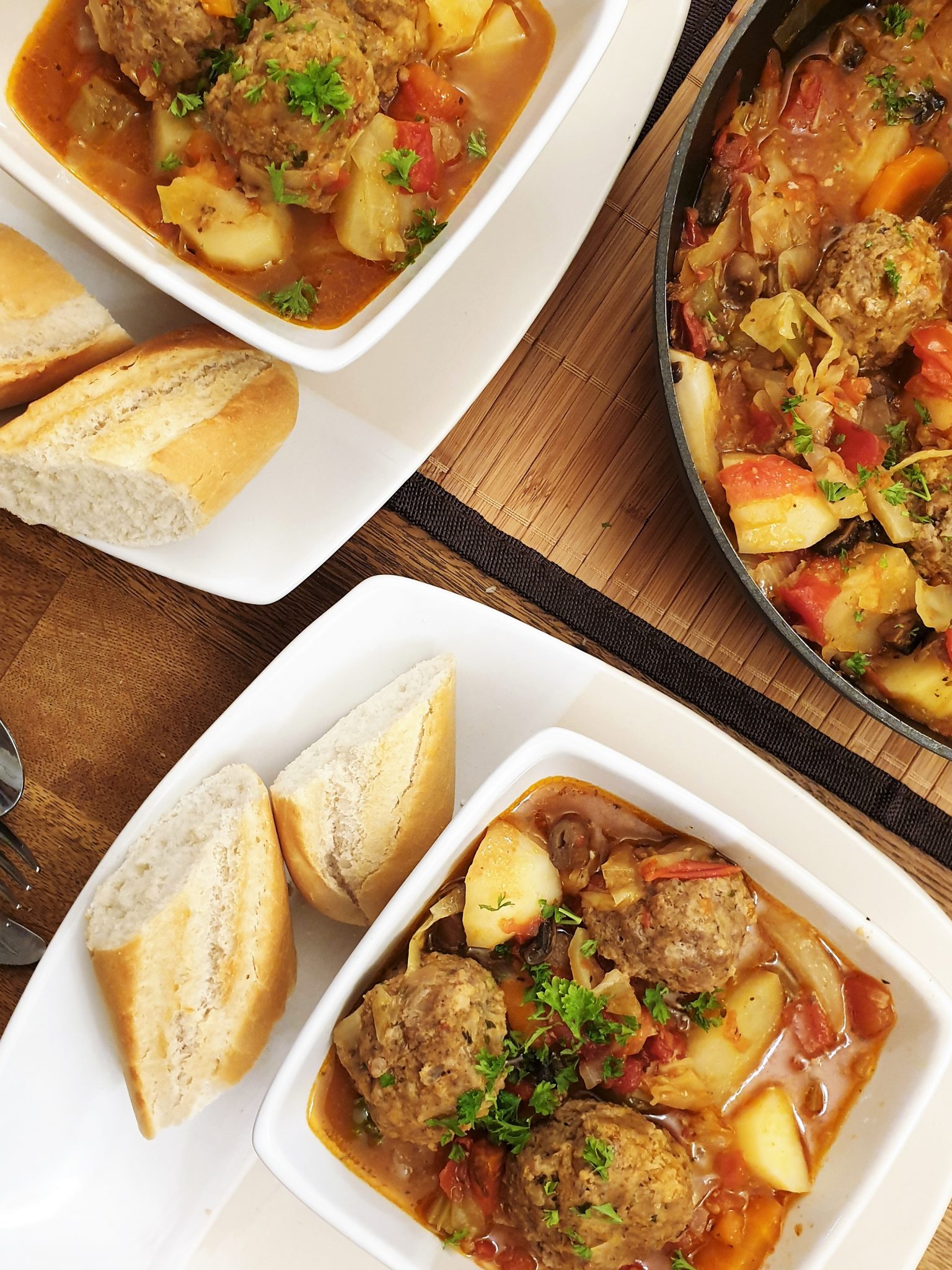 Overhead shot of 2 bowls of meatball and vegetable soup in dishes with crusty bread on the side.