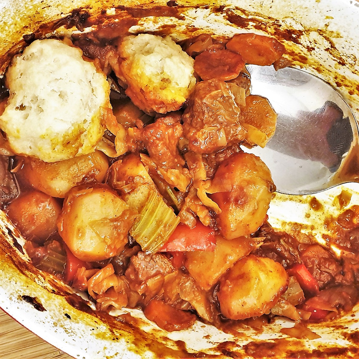 Closeup of the beef casserole and suet dumplings being spooned from the dish.