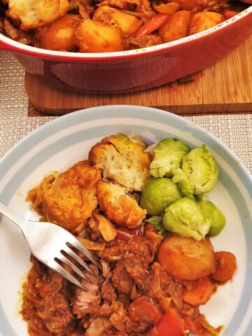 A plate of beef stew and dumplings showing the meat being shredded with a fork.