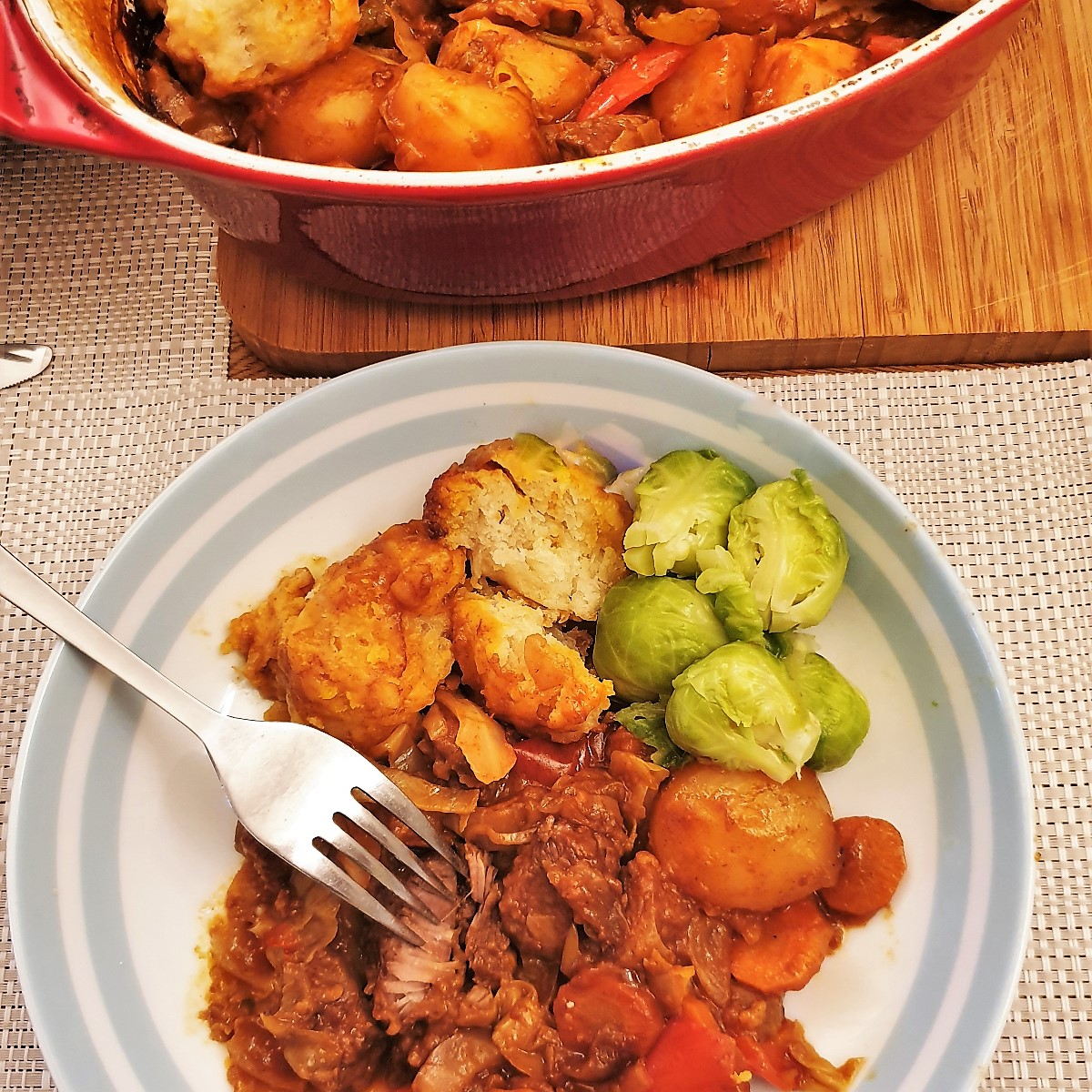 A dish of beef casserole and suet dumplings with a side helping of brussels sprouts.