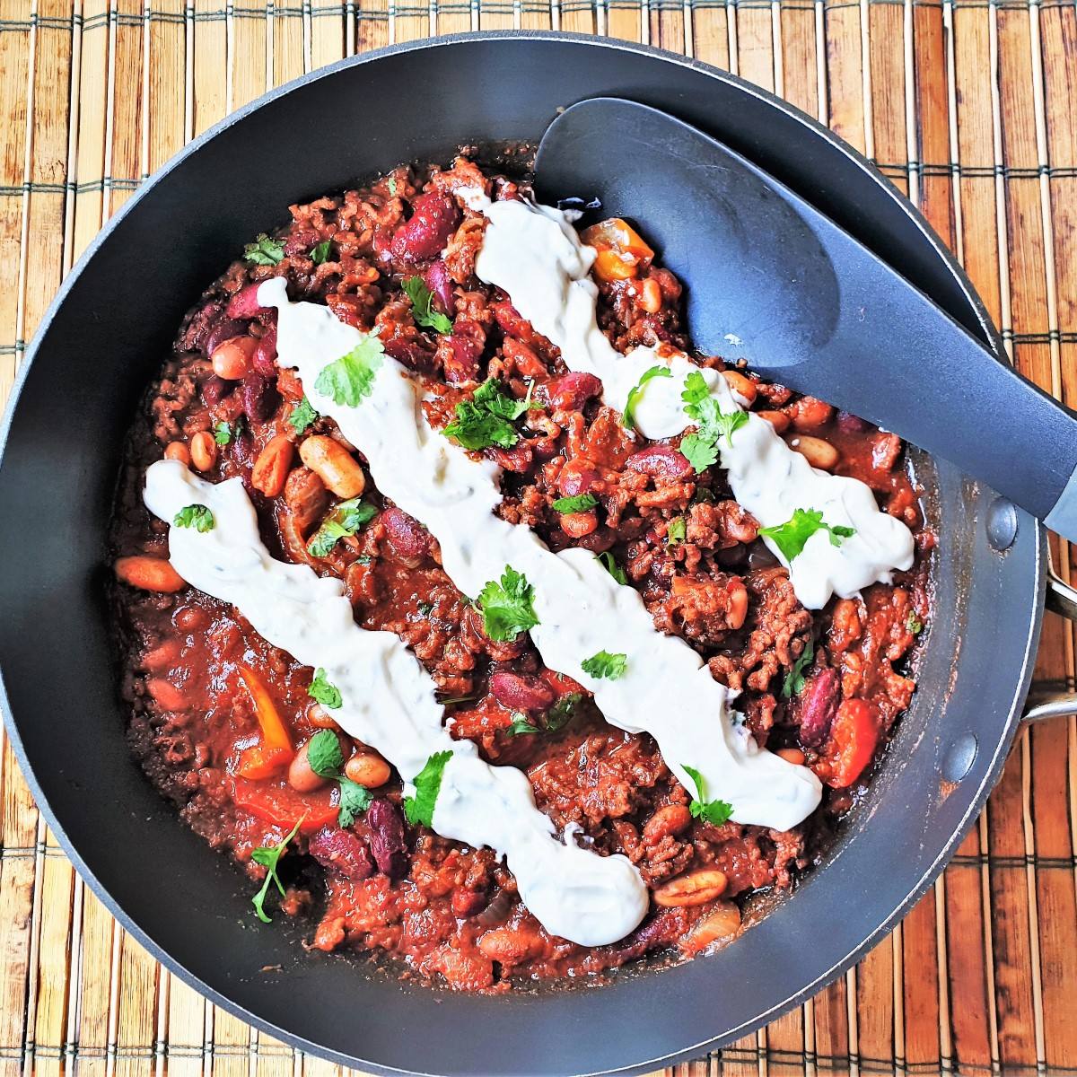 A pan of chilli with 3 rows of sour cream piped on top.