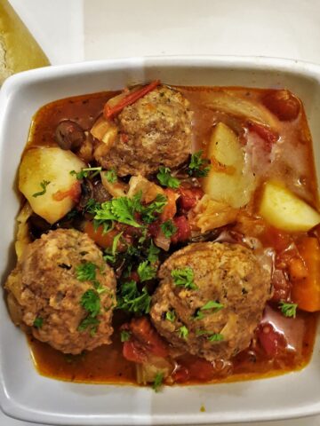 A dish of meatball soup with vegetables and tomatoes and custy bread.