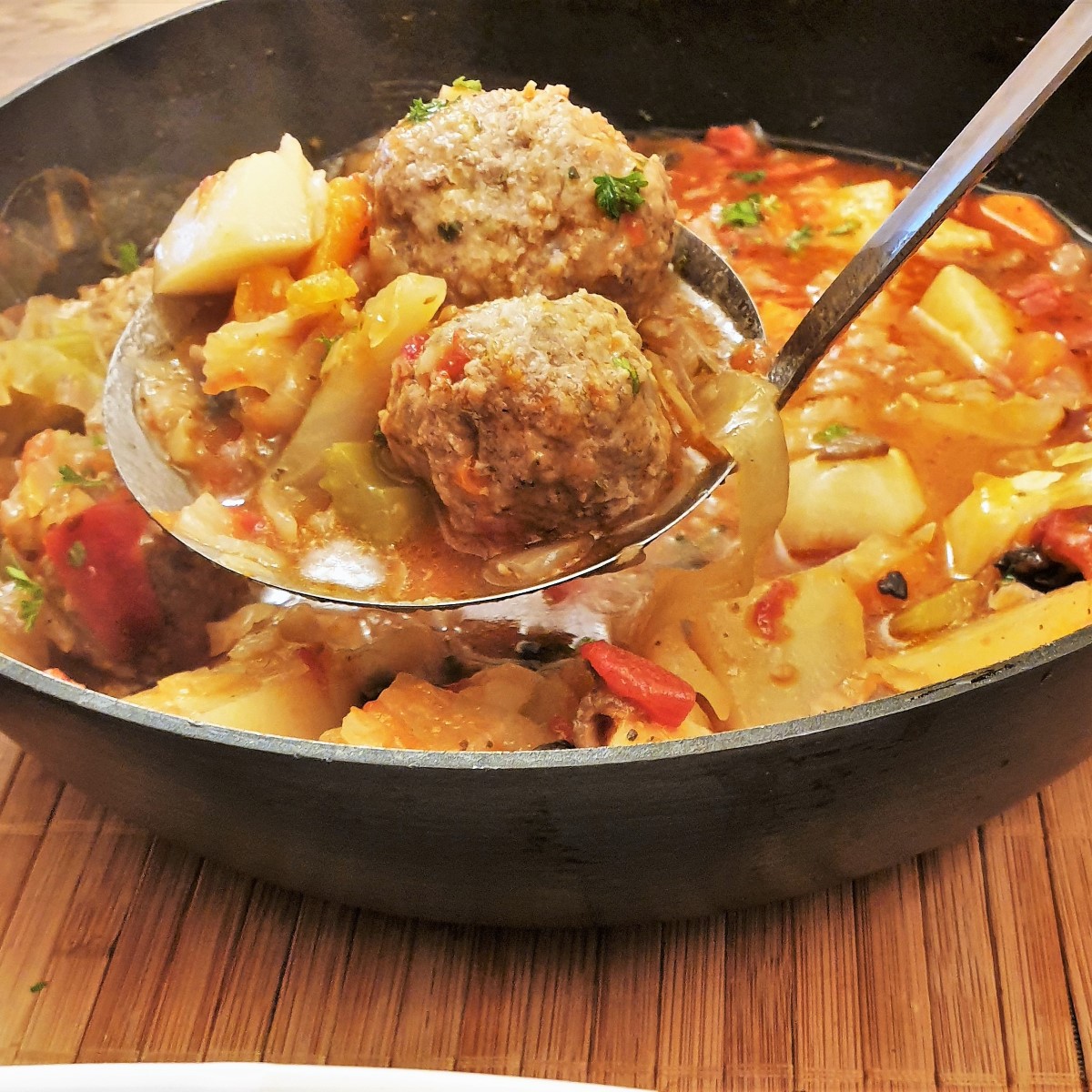 Meatballs being spooned from a pan of meatball and vegetable soup.