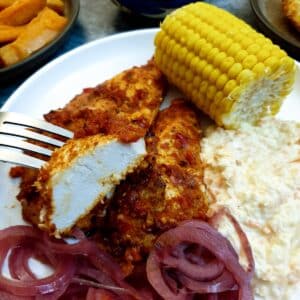 A piece of peri peri chicken with a cob of sweetcorn in the background.