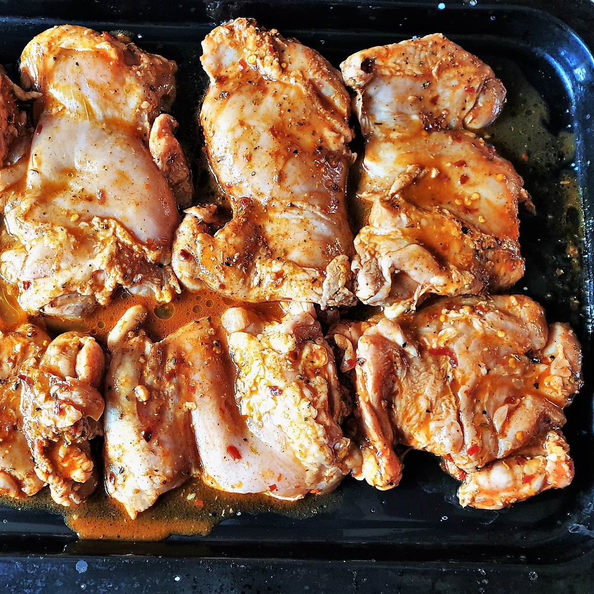 Raw marinaded chicken thighs on a baking tray.