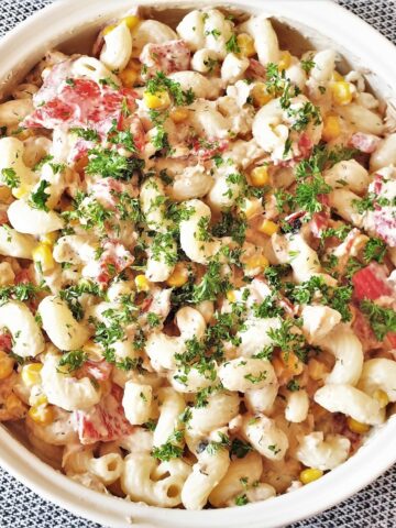 A bowl of salmon and red pepper pasta salad, sprinkled with chopped parsley.