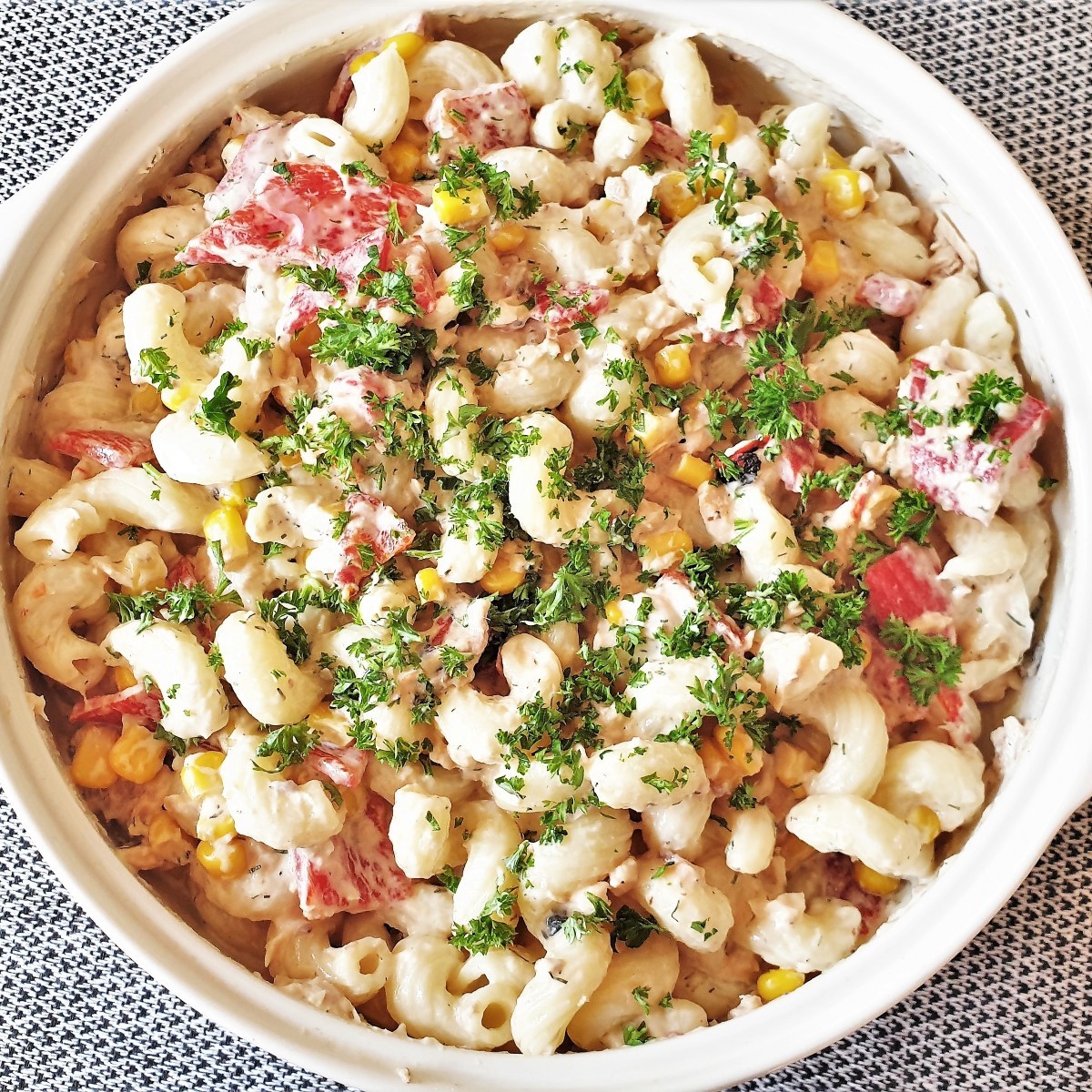 A bowl of salmon and red pepper pasta salad, sprinkled with chopped parsley.