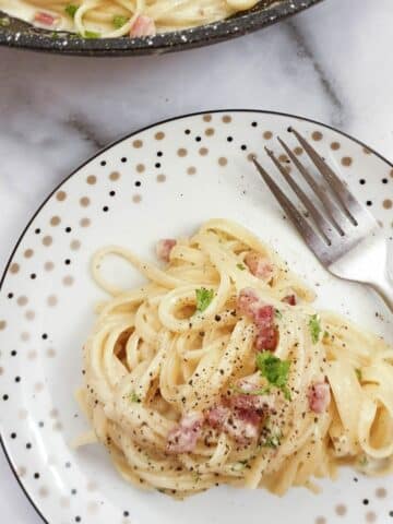 A plate of spaghetti carbonara sprinkled with black pepper.