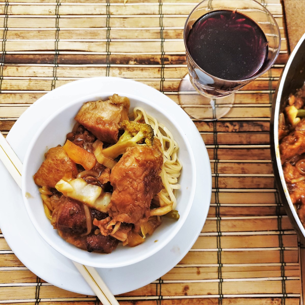 Overhead shot of a bowl of szechuan chicken next to a glass of red wine.