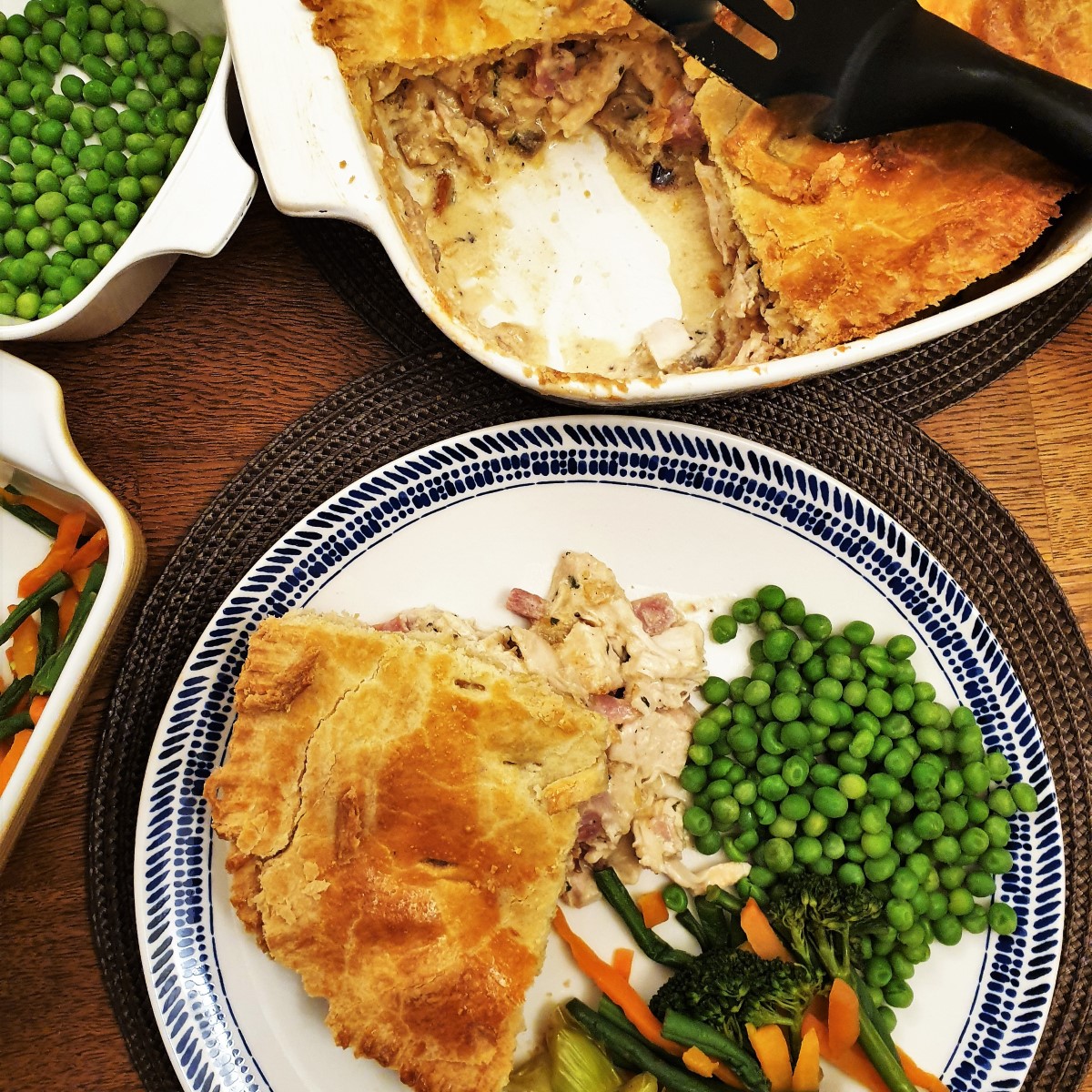 Overhead shot of a plate of chicken and ham pie  with vegetables, next to the dish of pie with a slice removed..