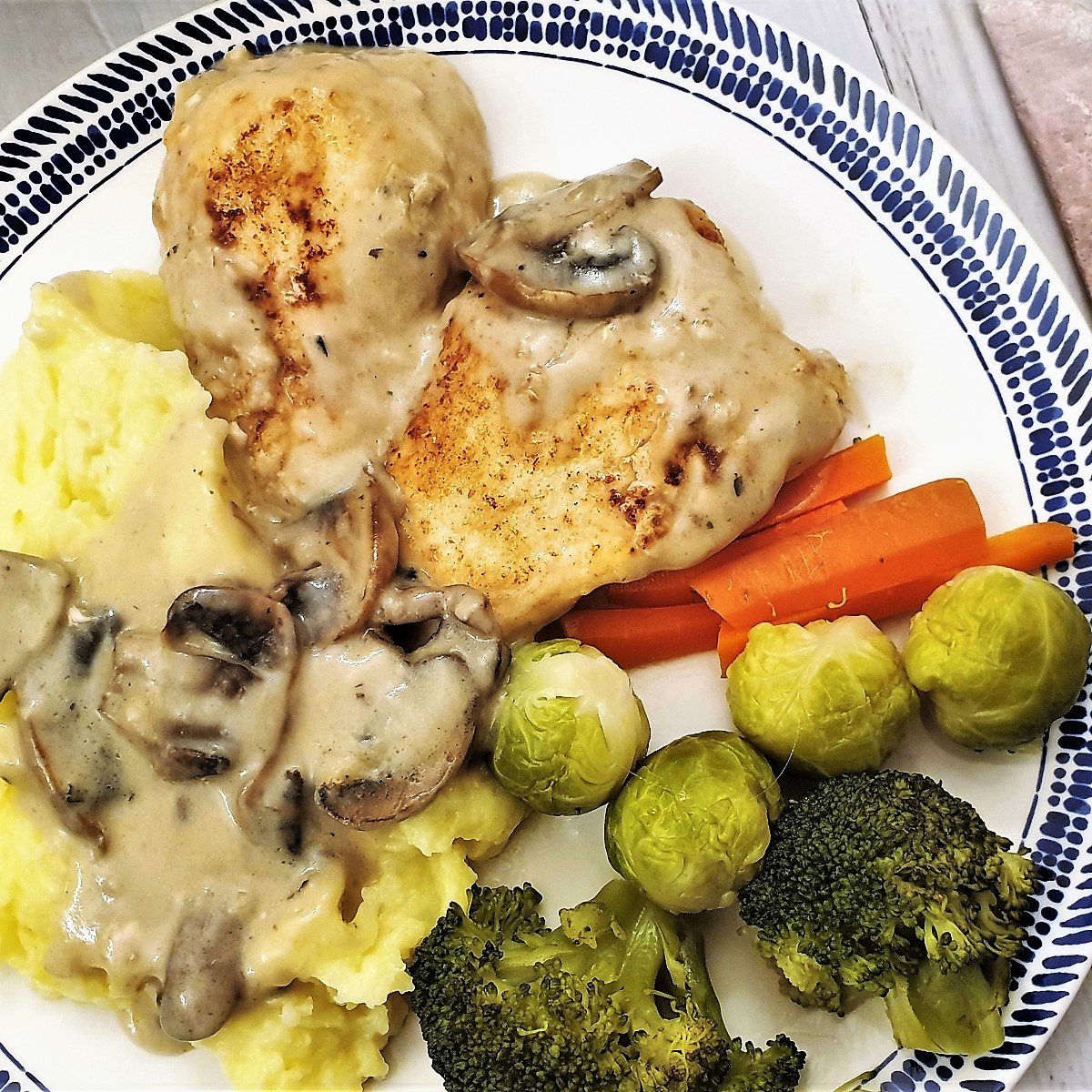 A plate of creamy chicken marsala with mushrooms, mashed potatoes and vegetables.