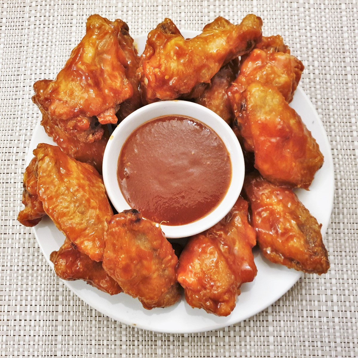 A plate of chicken wings surrounding a bowl of barbeque sauce.