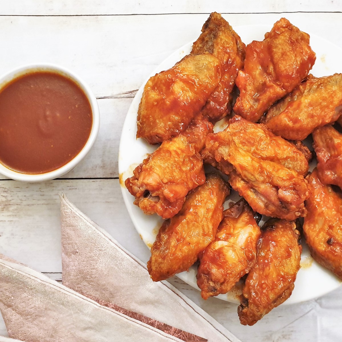 A pile of chicken wings next to a bowl of barbeque sauce.