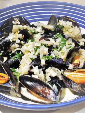 A dish of mussels covered in creamy garlic and onion sauce.