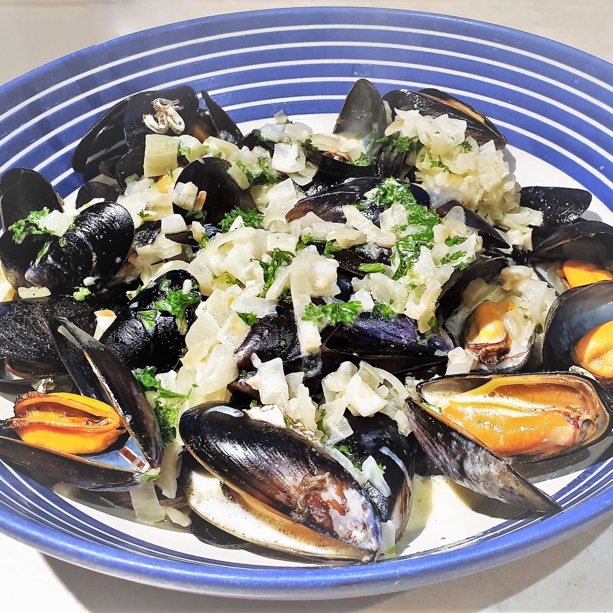 A dish of mussels covered in creamy garlic and onion sauce.