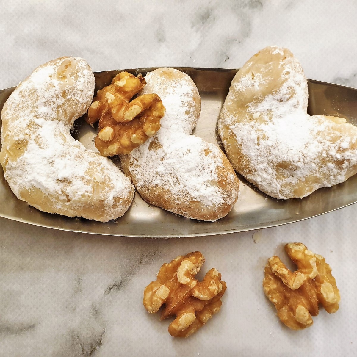 Three walnut crescent cookies on a small tray.