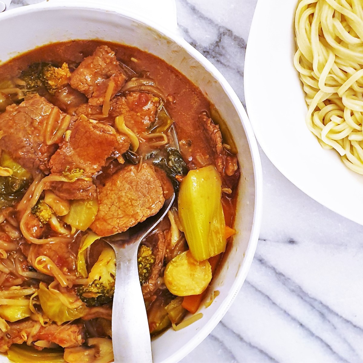 A dish of beef in oyster sauce alongside a dish of spaghetti noodles.