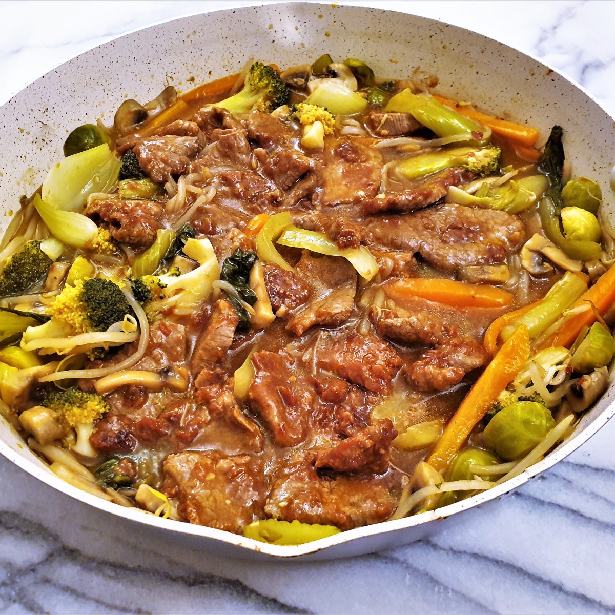 Side-on shot of a pan of garlic beef in oyster sauce with vegetables.