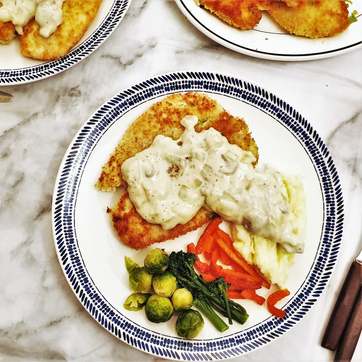 Overhead shot of a chicken schnitzel covered in creamy mushroom sauce, on a plate with vegetables.