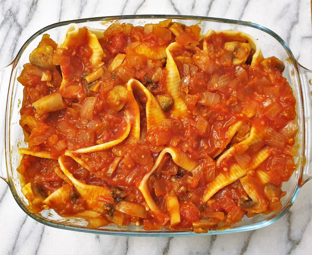 A baking dish filled with jumbo pasta shells and meatballs, covered with homemade tomato sauce.