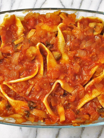 A baking dish filled with jumbo pasta shells and meatballs, covered with homemade tomato sauce.
