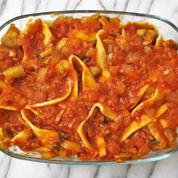 A baking dish filled with jumbo pasta shells and meatballs, covered with homemade tomato sauce.