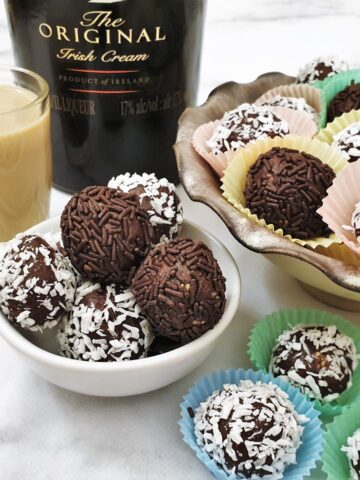 A dish of chocolate truffles, rolled in coocnut and chocolate sprinkles, in front of a bottle of Baileys.