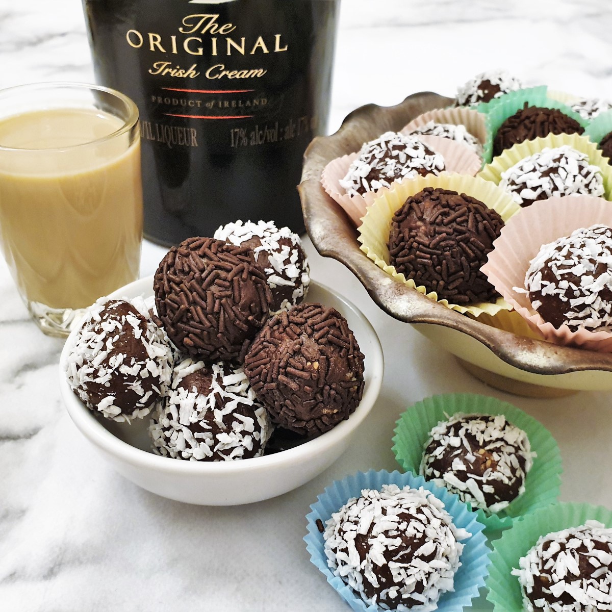 A dish of chocolate truffles, rolled in coocnut and chocolate sprinkles, in front of a bottle of Baileys.