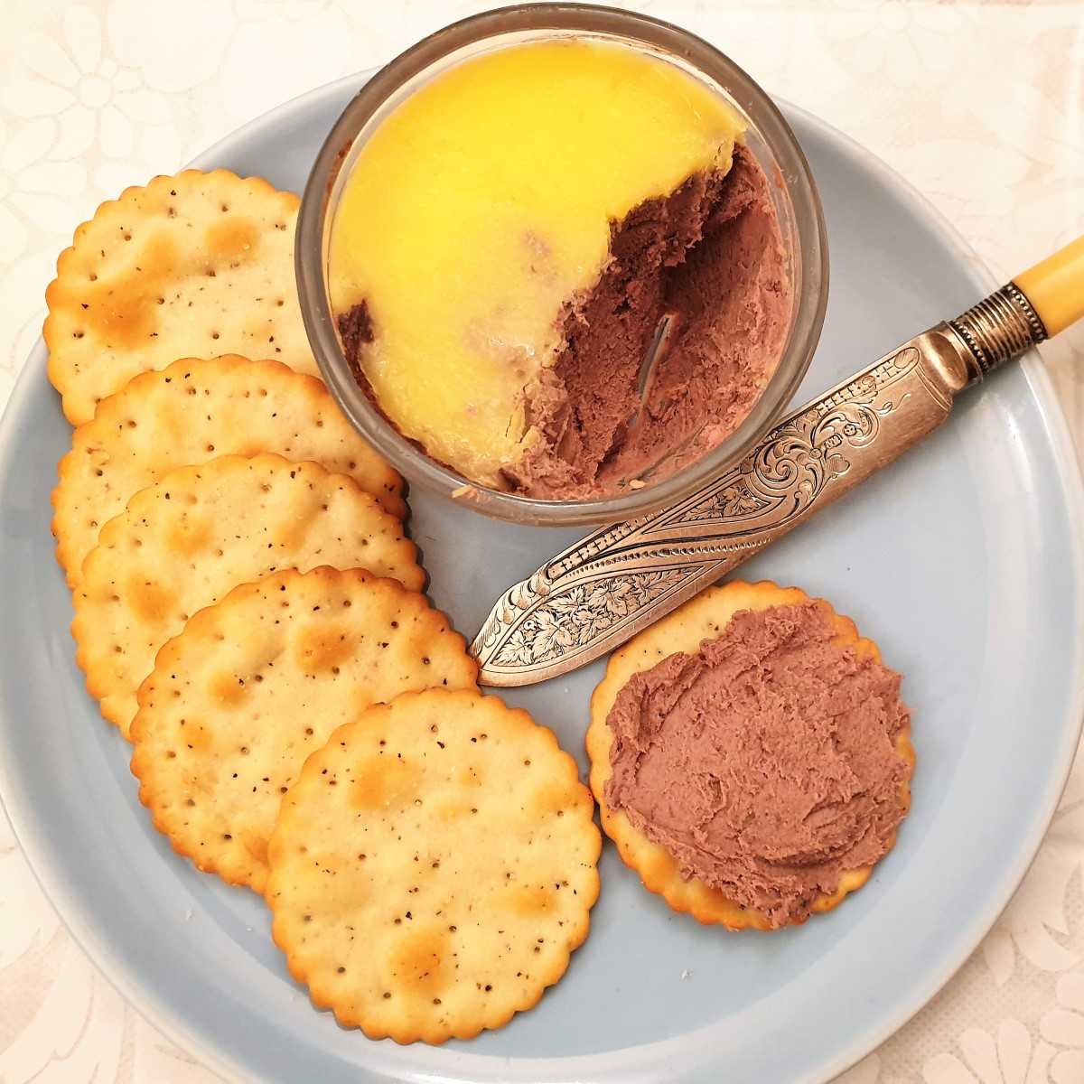 A dish of chicken liver pate on a plate with a biscuit spread with the pate.