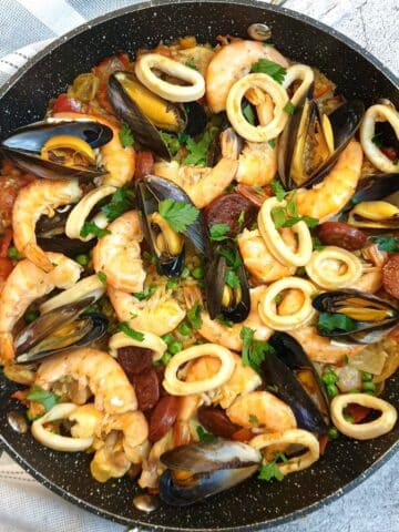 A pan of Spanish paella garnished with prawn, mussels and calamari rings.