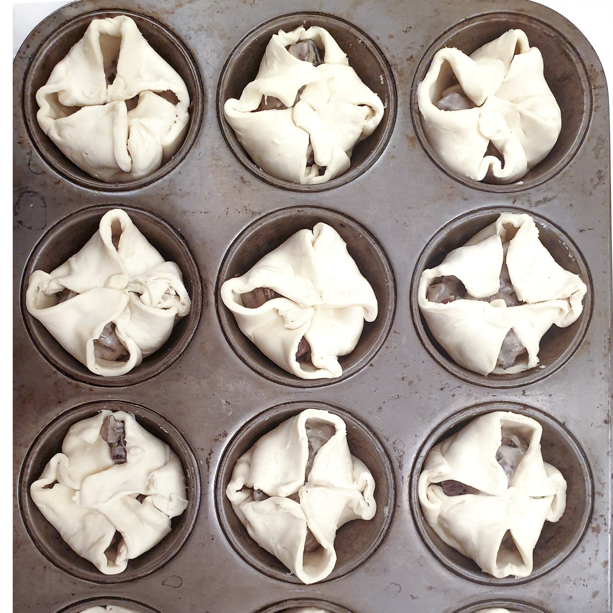 12 mini mushroom tarts in a muffin pan ready to go into the oven.