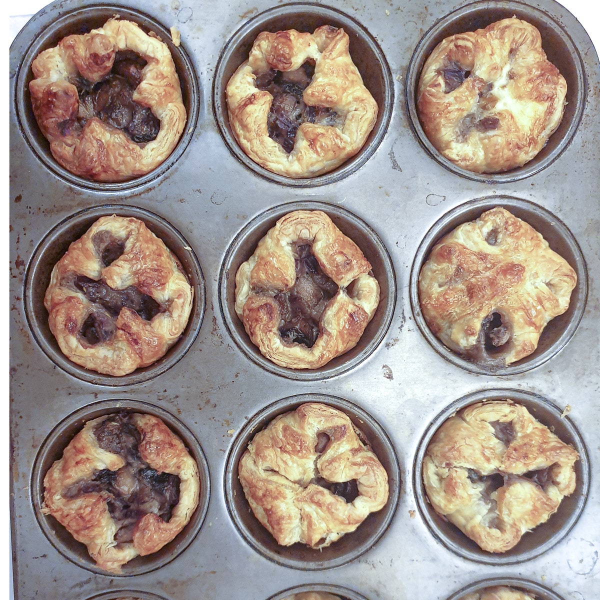 12 baked mikni mushroom puff pastry tarts cooling in a muffin pan.