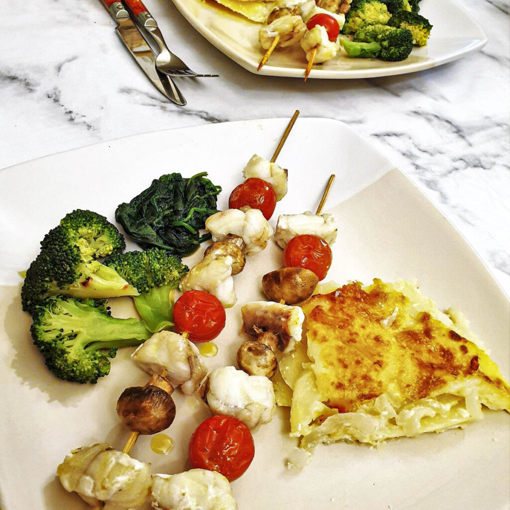 Monkfish kebabs on a plate with vegetables.