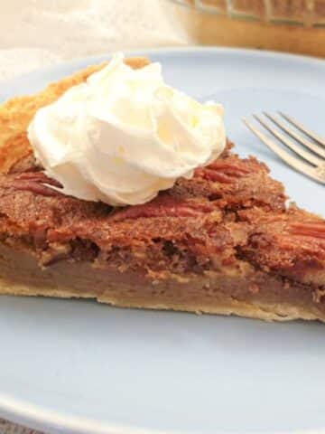 A slice of pecan nut pie, topped with cream, on a plate with a fork.