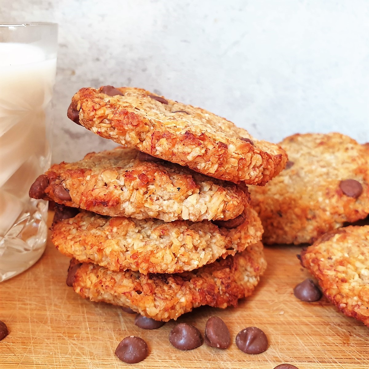 A pile of banana oat cookies next to a glass of milk.